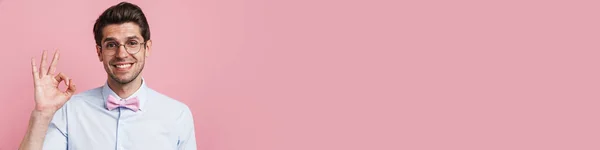 笑顔若いですブルネットオタク男身に着けているシャツと蝶立って上のピンクの壁の背景ショーOk — ストック写真