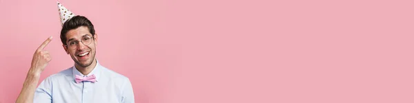 Jongeman Met Vlinderdas Wijzende Vinger Naar Feestkegel Glimlachend Geïsoleerd Roze — Stockfoto
