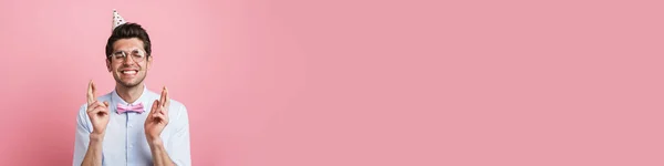 Jongeman Draagt Strikje Feestkegel Met Vingers Gekruist Geïsoleerd Roze Achtergrond — Stockfoto
