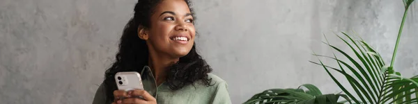 Musta Nuori Nainen Käyttää Matkapuhelinta Istuessaan Nojatuolissa Sisätiloissa — kuvapankkivalokuva