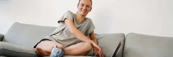 Χαμογελαστή Νεαρή Λευκή Ανάπηρη Γυναίκα Προστατευτικό Πόδι Κάθεται Έναν Καναπέ — Φωτογραφία Αρχείου