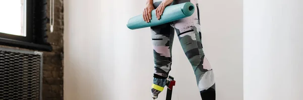 stock image Young sportswoman with prosthesis posing with fitness mat indoors