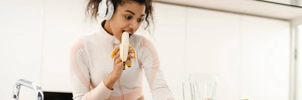 Black Woman Headphones Using Laptop While Making Smoothie Home Stock Photo