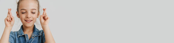 Blonde white girl in denim shirt holding fingers crossed for good luck isolated over white background