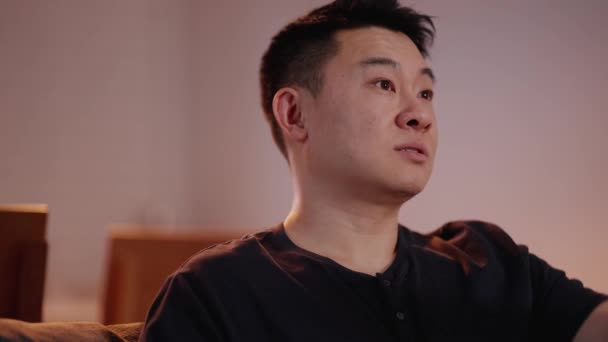 Koncentrerad Asiatisk Man Tittar Och Pratar Soffan Hemma — Stockvideo
