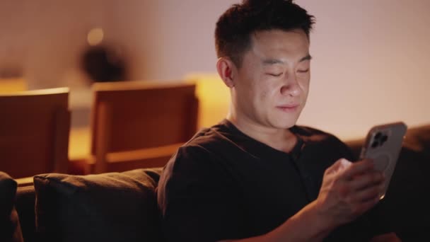 Pozytywny Azjatycki Mężczyzna Smsy Smartfonie Kanapie Nocy — Wideo stockowe