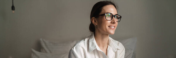 Smiling mid aged brunette white businesswoman sitting on bed in a hotel room holding mobile phone