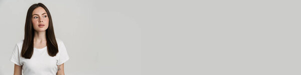 Молодая брюнетка в футболке позирует и смотрит в сторону изолированы на белом фоне