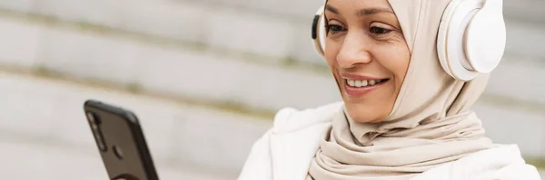 Senyum Setengah Baya Muslim Wanita Headphone Memegang Ponsel Berdiri Jalan — Stok Foto
