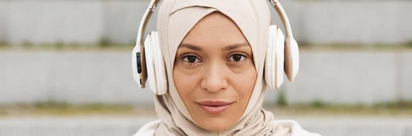 中东妇女头戴头巾 在室外用无线耳机听音乐 — 图库照片