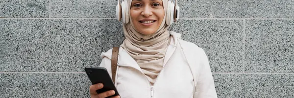 中东妇女头戴头巾 在室外用耳机和手机听音乐 — 图库照片