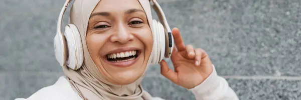 Lähi Idän Nainen Hijabissa Nauraa Kuunnellessaan Musiikkia Langattomilla Kuulokkeilla Ulkona — kuvapankkivalokuva