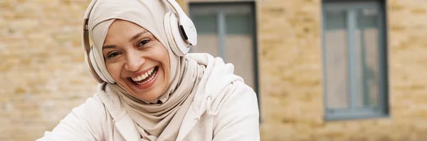 Lähi Idän Nainen Hijabissa Kuuntelemassa Musiikkia Kuulokkeilla Istuessaan Ulkona — kuvapankkivalokuva