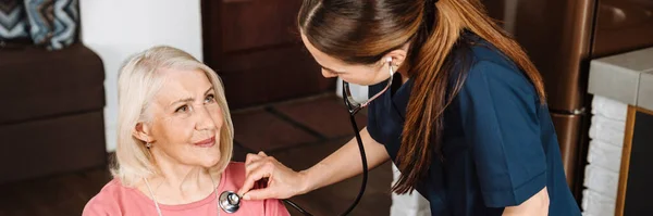 Naislääkäri Joka Kuuntelee Stetoskoopilla Iäkästä Potilasta Kotona — kuvapankkivalokuva