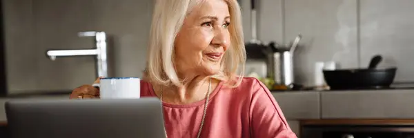 Concentrated Elderly Woman Cup Her Hands Working Laptop Looking Side — Stock Photo, Image
