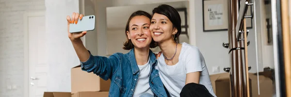 Hymyilevä Lesbo Pari Tytöt Tekevät Selfie Puhelimessa Istuessaan Lattialla Huoneessa — kuvapankkivalokuva