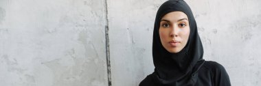 Başörtülü genç Müslüman kadın su şişesiyle içeride duruyor.