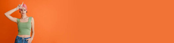 Молодая белая женщина с розовыми волосами, указывая пальцем вверх на оранжевый фон