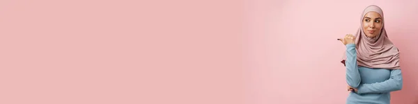 Позитивная Мусульманка Розовом Хиджабе Указывающая Копировальное Пространство Смотрящая Сторону Розовой — стоковое фото