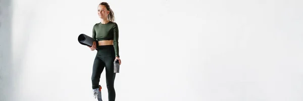 Ung Sportskvinne Med Protese Som Holder Fitnessmatte Vannflaske Isolert Hvit – stockfoto