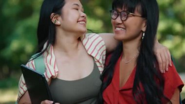 Gülümseyen Asyalı kız öğrenciler yazın kucaklaşıp dışarıyı seyrediyorlar.