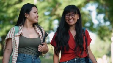 Gülümseyen Asyalı kız öğrenciler yazın dışarıda yürürken konuşuyorlar.