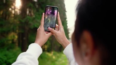 Kadının arkadan görünüşü ormanın fotoğrafını çekiyor. Telefonuyla dışarı çıktıktan sonra.