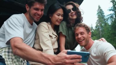 Dağlarda bir arabanın bagajında cep telefonu kamerasıyla selfie çeken çok uluslu komik arkadaşlar.