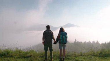 Sırt çantalarıyla dağda yürüyüş yapan ve sisin içindeki manzaraya bakan çiftin arka görüntüsü. Kamp kavramı
