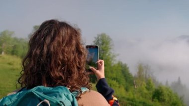 Kıvırcık saçlı kadın cep telefonu kamerasıyla dağları çekiyor. Kamp kavramı