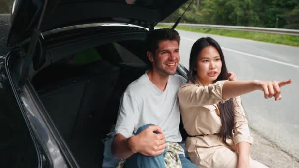 Cute Wielonarodowa Para Rozmawia Wskazuje Widok Siedząc Bagażniku Samochodu Górach — Wideo stockowe