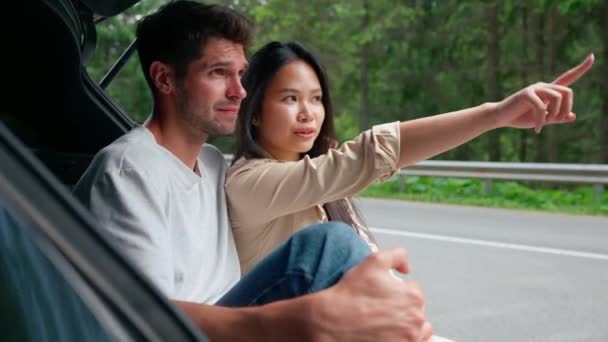 Piękna Wielonarodowa Para Rozmawia Wskazuje Widok Siedząc Bagażniku Samochodu Górach — Wideo stockowe