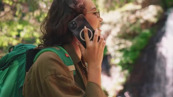 Усміхнена Туристична Жінка Сонцезахисних Окулярах Говорить Телефону Проти Водоспаду Горах — стокове відео