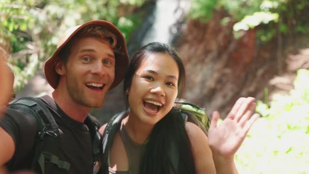 Sonriente Pareja Turista Multinacional Grabando Vídeo Cámara Saludando Contra Cascada — Vídeo de stock
