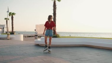 Güneş gözlüklü genç bir kadın denizin kenarında paten kayıyor.