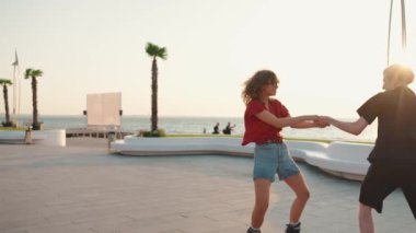 Deniz kenarında paten kayarken el ele tutuşan güzel genç bir çift.