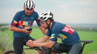 Bisikletli iki sporcu yolda bisiklet sürdükten sonra telefonla mesajlaşıyor.