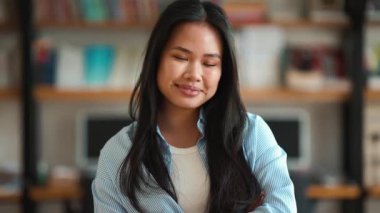 Neşeli Asyalı genç kız öğrenci kütüphanede kameraya bakıyor.