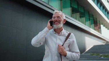 Gülümseyen takım elbiseli bir işadamı işe giderken cep telefonuyla konuşuyor.