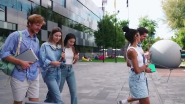 Çok uluslu genç öğrenciler yaz mevsiminde üniversitenin yakınlarında konuşuyor ve merdivenlerden iniyorlar.