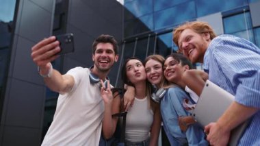 Üniversitenin yakınlarında cep telefonuyla selfie çeken gülümseyen çok uluslu genç öğrenciler.