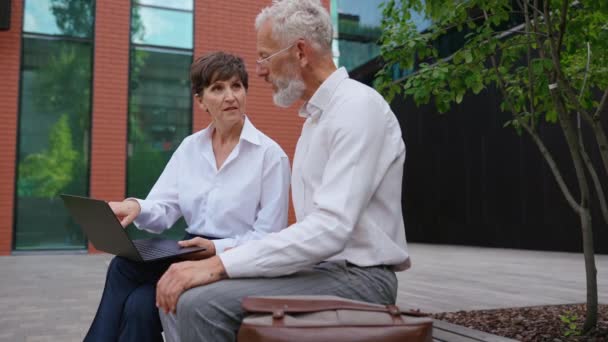 外のベンチに座っている間 ラップトップの仕事について話し合うことを正式に着用している高齢者ビジネスの人々 — ストック動画