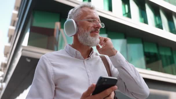 ポジティブな高齢のビジネスマンは 携帯電話を見て 働く方法で音楽を聞いているスーツで — ストック動画