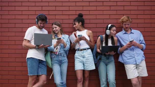 夏のレンガの壁の近くで携帯電話やラップトップを入力する驚異的な多文化の若い学生 — ストック動画