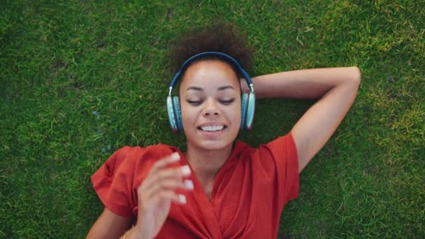 Довольно Африканская Женщина Слушает Музыку Наушниках Лежащих Траве Открытом Воздухе — стоковое видео