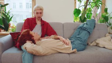 Evdeki kanepede konuşan boyalı saçlı, gülen genç eşcinsel çift.