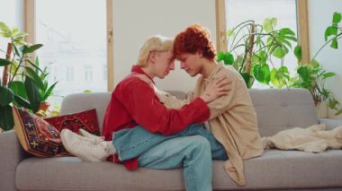 Saçları boyalı ve evdeki kanepede birbirlerine bakan sevimli eşcinsel çiftin yan görüntüsü.