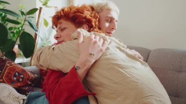 Evdeki kanepede boyalı saçlı neşeli eşcinsel çiftin yan görünüşü.