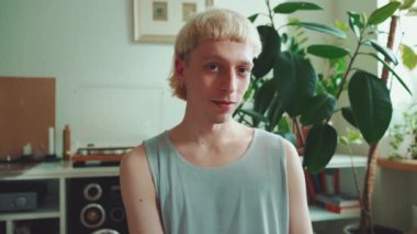 Güzel, genç, eşcinsel, sarışın, boyalı saçlı adam evdeki yatakta kameraya bakıyor.