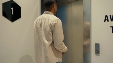 Olumlu genç Afrikalı adam asansörü arıyor ve ofisteki cep telefonuna bakıyor.